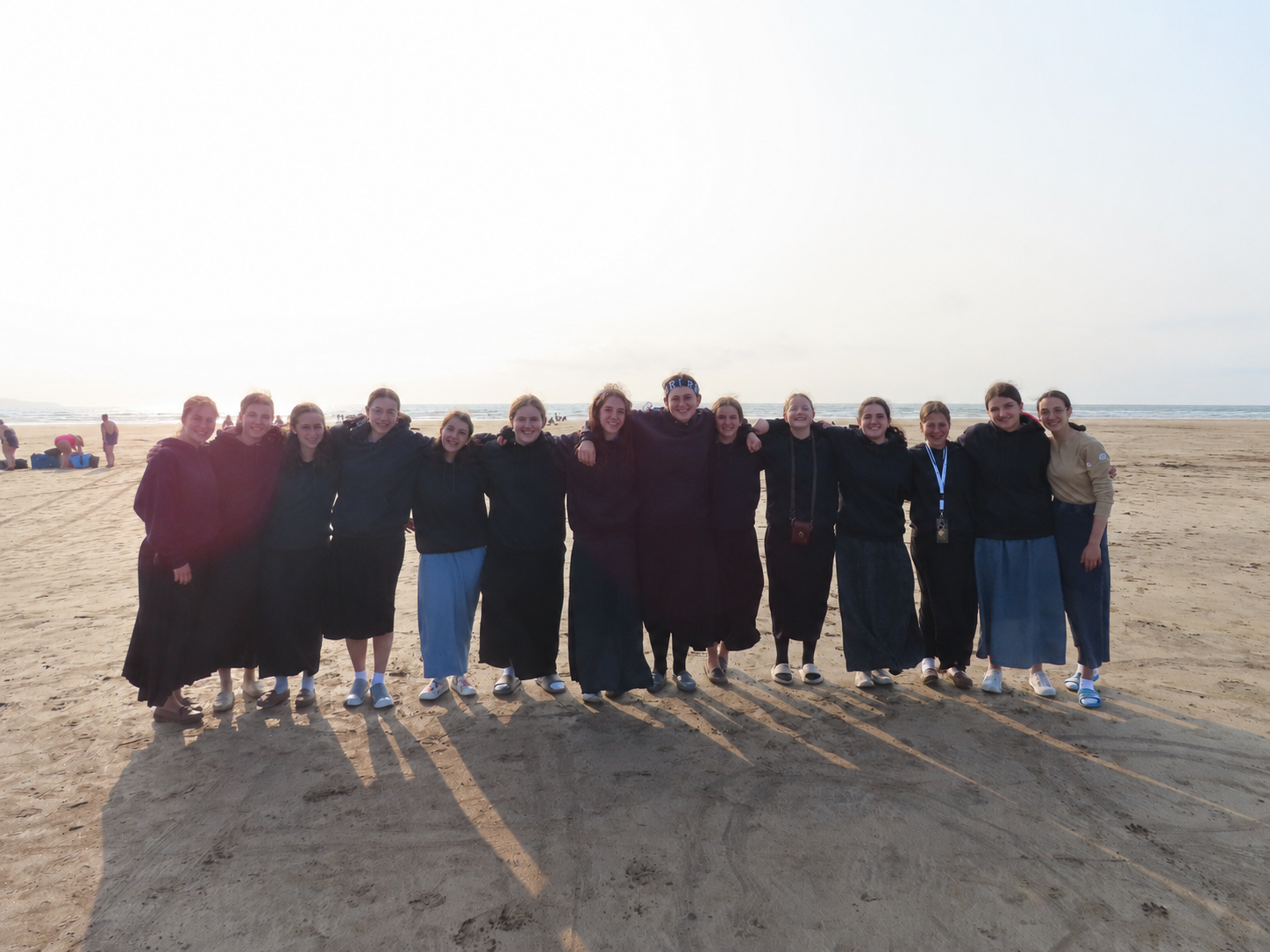 A group of girls standing together on a beach in the sunlight.